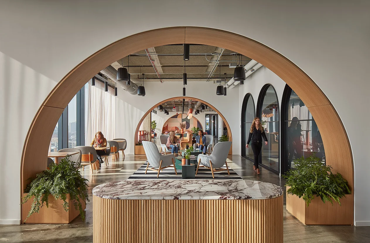 Stylish lounge area inside Google Chicago office with wooden archways, plants, and people working in a modern open space.