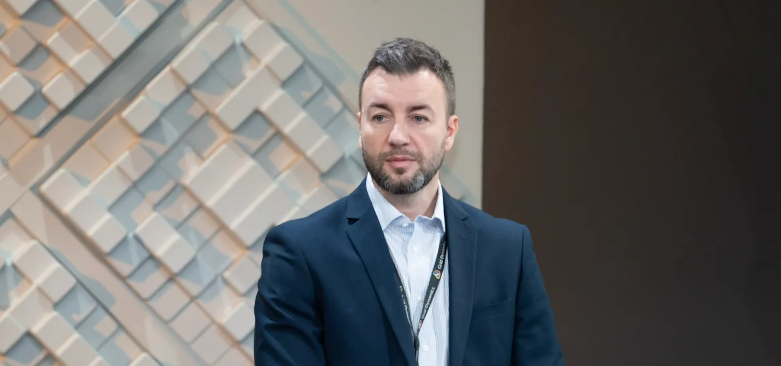 Man in a suit standing in front of a geometric wall panel.
